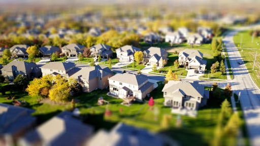 Tilt-shift aerial photo of a suburban neighborhood with green lawns and roads.